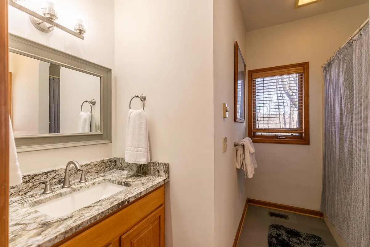 A bright and refreshing bathroom space with a granite countertop, a large mirror, and a window allowing natural light to filter in. The soothing environment is ideal for morning routines or relaxing after a long day.