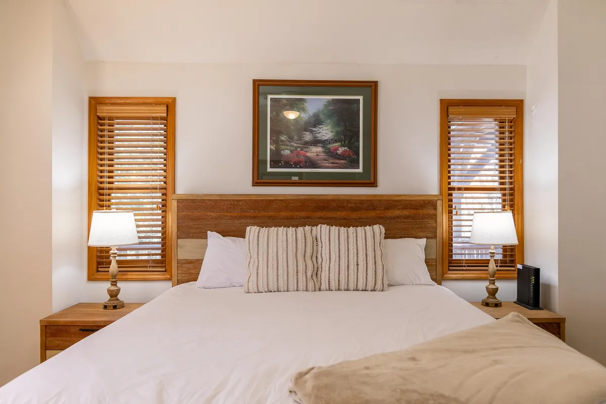 A tranquil king suite featuring a plush bed with soft linens, flanked by matching nightstands and lamps. Framed artwork adds a touch of elegance, and natural morning light gently fills the space, creating a peaceful retreat ideal for restful nights or quiet reading.