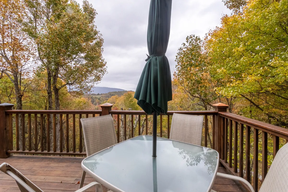 An exterior view of a table with a glass top and umbrella, set amidst lush greenery and trees. The setting is tranquil and private, emphasizing the peaceful atmosphere of the gated community while inviting guests to enjoy the outdoor environment in any weather.