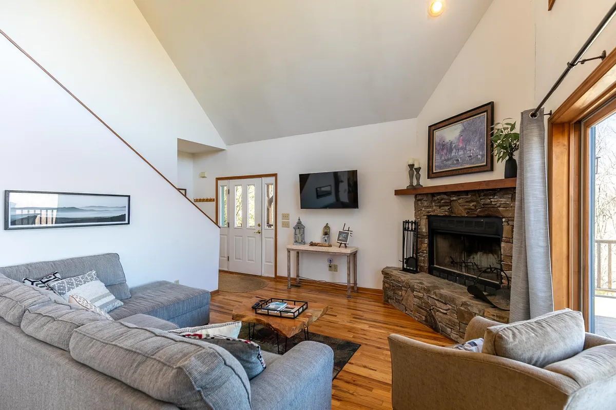 A cozy living space with a plush sofa, warm fireplace, coffee table, and a television, all framed by large windows that let in natural light. The atmosphere encourages relaxation, games, or movie nights with friends.