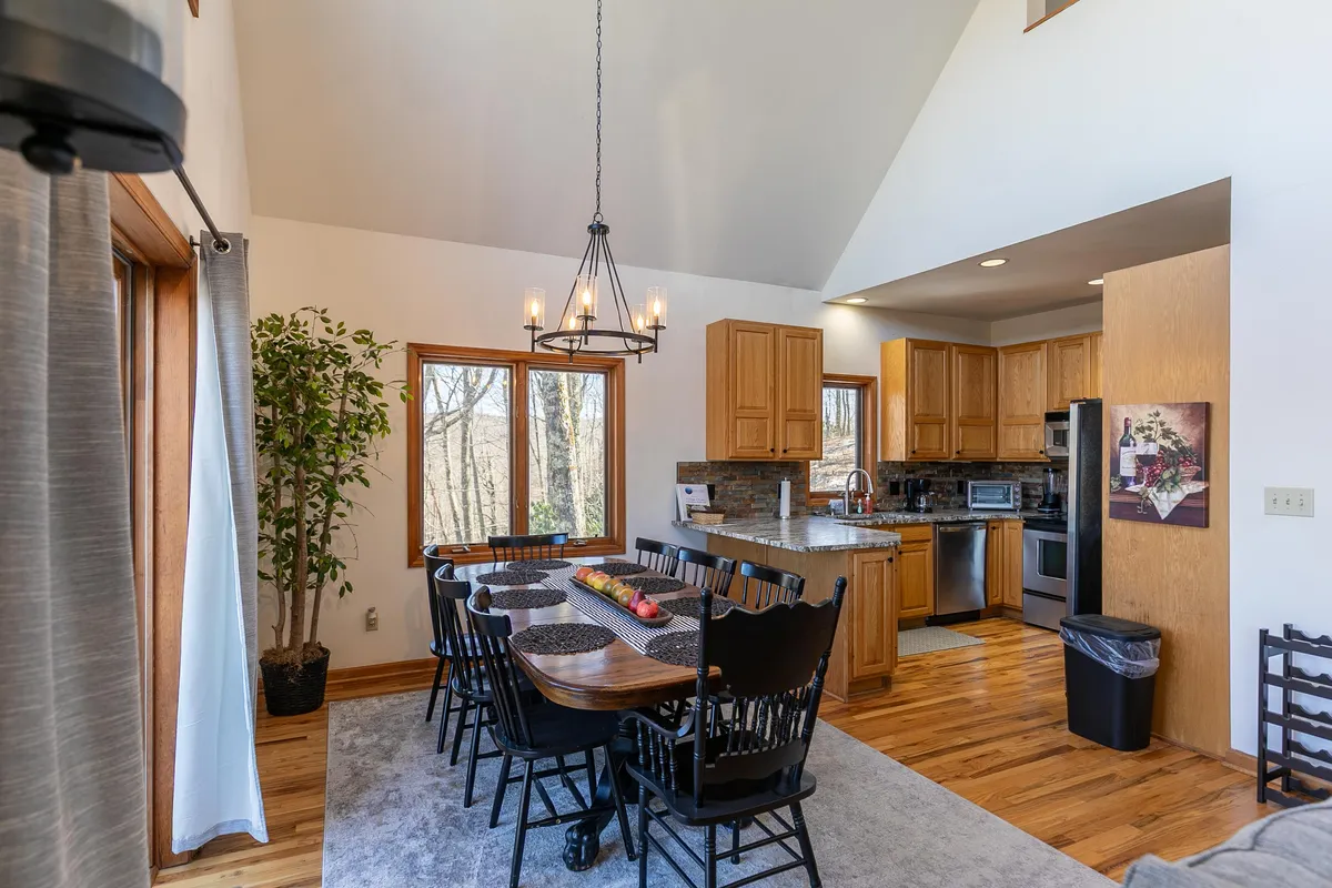This image provides a clear view of the spacious dining table set for eight, surrounded by large windows and adjacent to the open kitchen cabinetry. The setting is ideal for family meals or festive gatherings, with a warm and welcoming mood enhanced by natural light.
