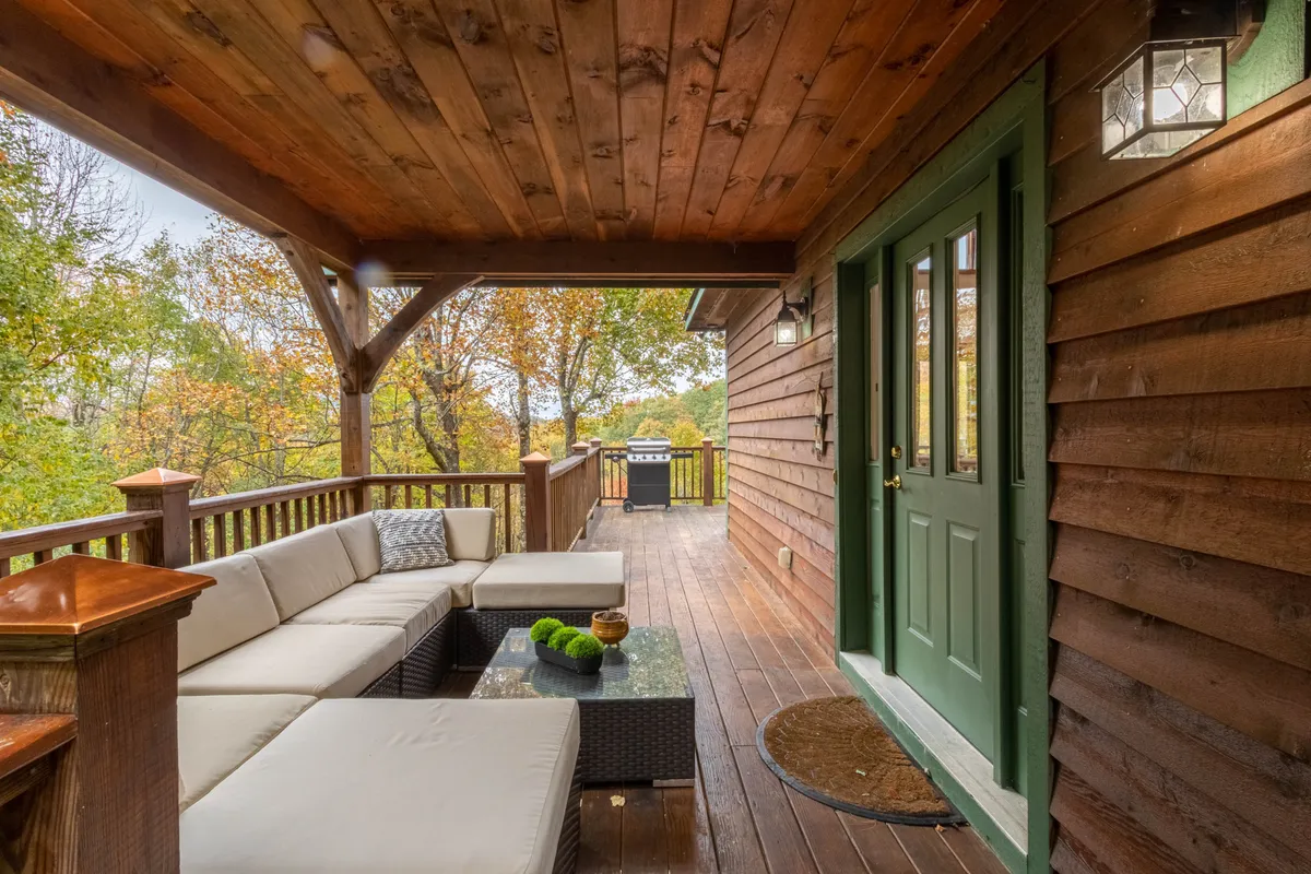 A welcoming outdoor seating area is set on a wooden deck, featuring a comfortable patio couch set near a green door. The view extends to surrounding trees, giving a sense of privacy and tranquility. The space is easily accessible and the surfaces are simple to maintain, making it ideal for pet owners.