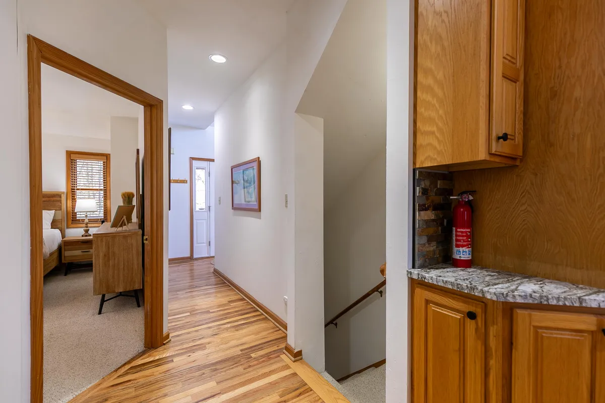 This interior image captures the welcoming entryway and central living space, featuring a wooden staircase, granite countertop, and artwork adorning the walls. The visible door to a bedroom hints at the home's flexible sleeping arrangements. The scene exudes a sense of warmth, comfort, and communal gathering.
